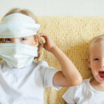 Portrait of two sisters putting on medical protective masks. The older sister helps the younger. Sisters playing fun. Coronavirus protection concept, quarantine. High quality photo
